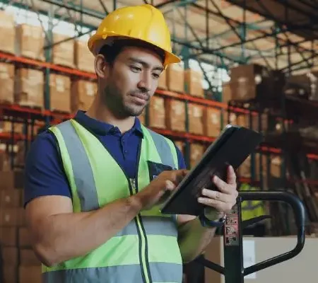 A worker in a hardhat manages crusher parts inventory with an ipad.