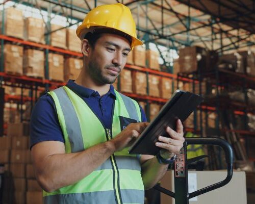 A worker in a hardhat manages crusher parts inventory with an ipad.