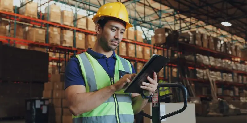 A worker in a hardhat manages crusher parts inventory with an ipad.