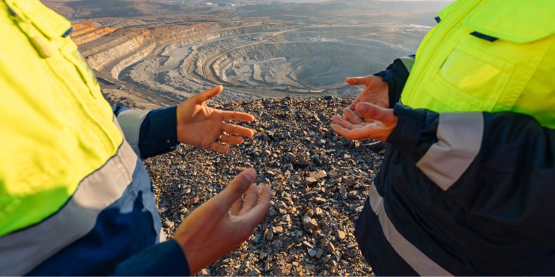 Two workers hands gesture as they talk above a quarry, discussing OEM crusher replacement parts