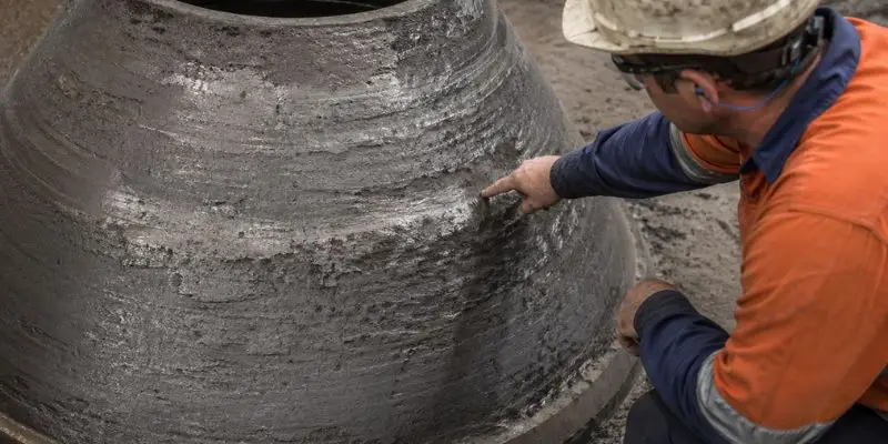 Technician inspecting worn cone crusher liner surface to assess wear patterns and support crusher liner optimization.