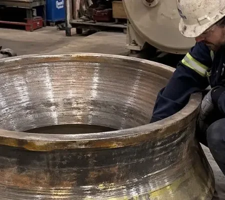 Technician inspecting cone crusher liner in a workshop to evaluate wear patterns and support crusher liner wear analysis.
