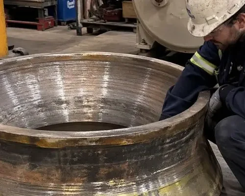 Technician inspecting cone crusher liner in a workshop to evaluate wear patterns and support crusher liner wear analysis.