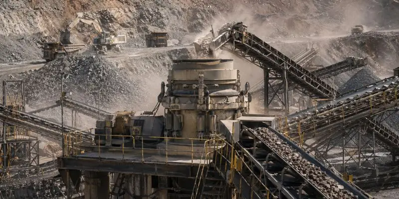Cone crusher operating at a large mining site with conveyors moving material, supporting efforts to reduce crusher downtime.