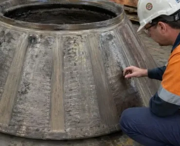 Technician inspecting worn cone crusher wear parts on large liner component in workshop