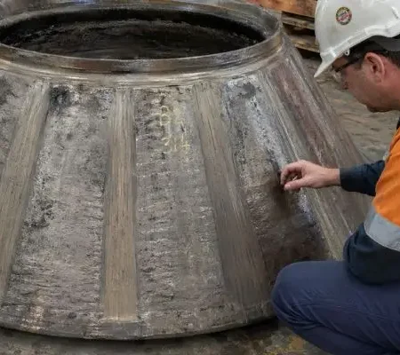 Technician inspecting worn cone crusher wear parts on large liner component in workshop