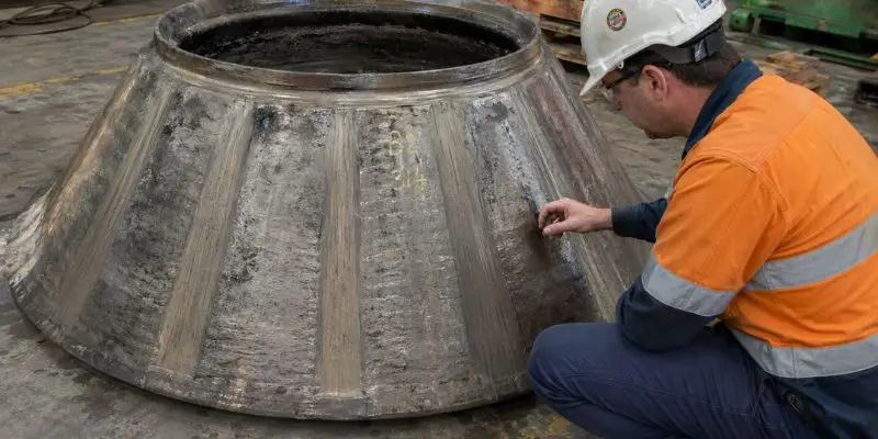 Technician inspecting worn cone crusher wear parts on large liner component in workshop