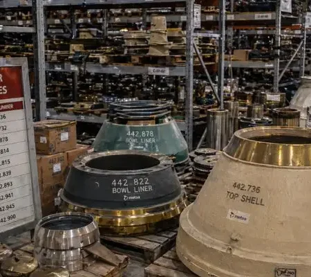 Warehouse stocked with mining crusher parts including mantles, bowl liners, and cone crusher components