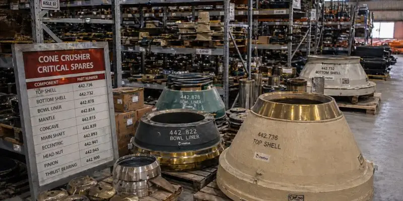 Warehouse stocked with mining crusher parts including mantles, bowl liners, and cone crusher components